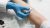 Nahaufnahme eines Pricktests zur Allergiediagnostik (Draufsicht). Eine Hand mit blauen, medizinischem Einmalhandschuh träufelt Allergenlösung aus einer kleinen weißen Flasche auf die Innenseite des Unterarms einer Patientin, auf das dafür vorgesehene gezeichnete Feld. Auf dem Arm sind Kästchen mit den Zahlen 1-9 aufgemalt. Im Anschnitt des Fotos sind zudem mehrere leere Reagenzgläser in Halterungen sichtbar.