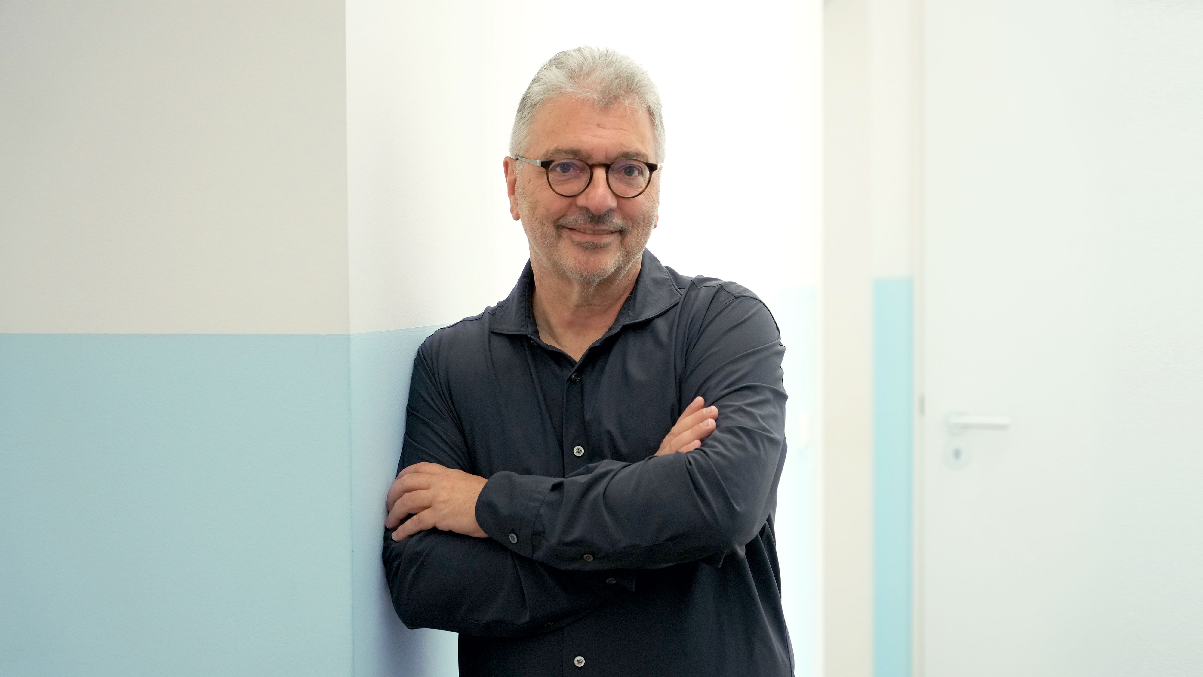 Freundliches Porträt des leitenden Arztes Dr. med. Andreas Forster im Praxisflur des Lungenzentrums Darmstadt an die Wand gelehnt