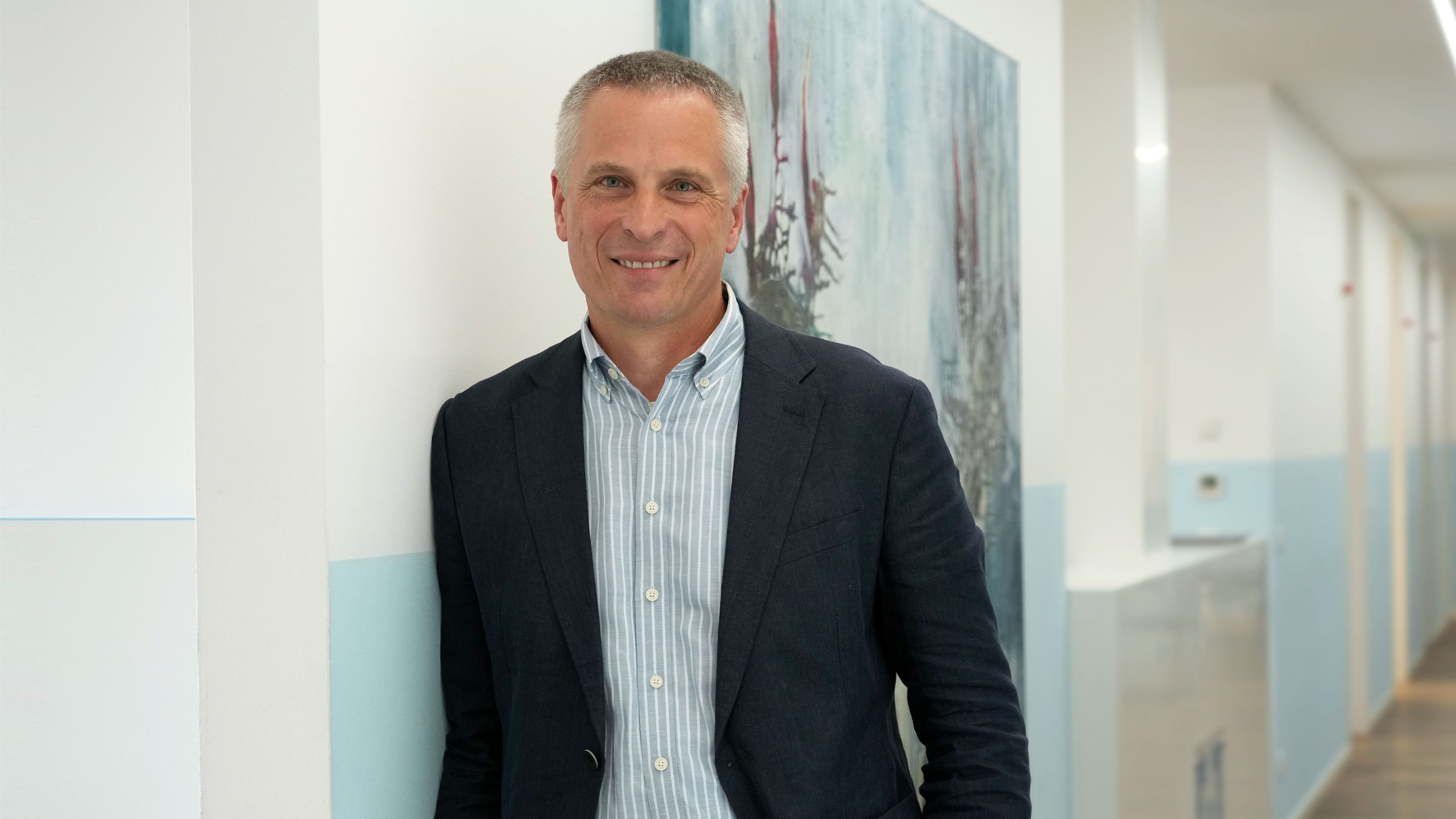 Freundliches Porträt des leitenden Arztes Dr. med. Konrad Kneser im Praxisflur des Lungenzentrums Darmstadt an die Wand gelehnt