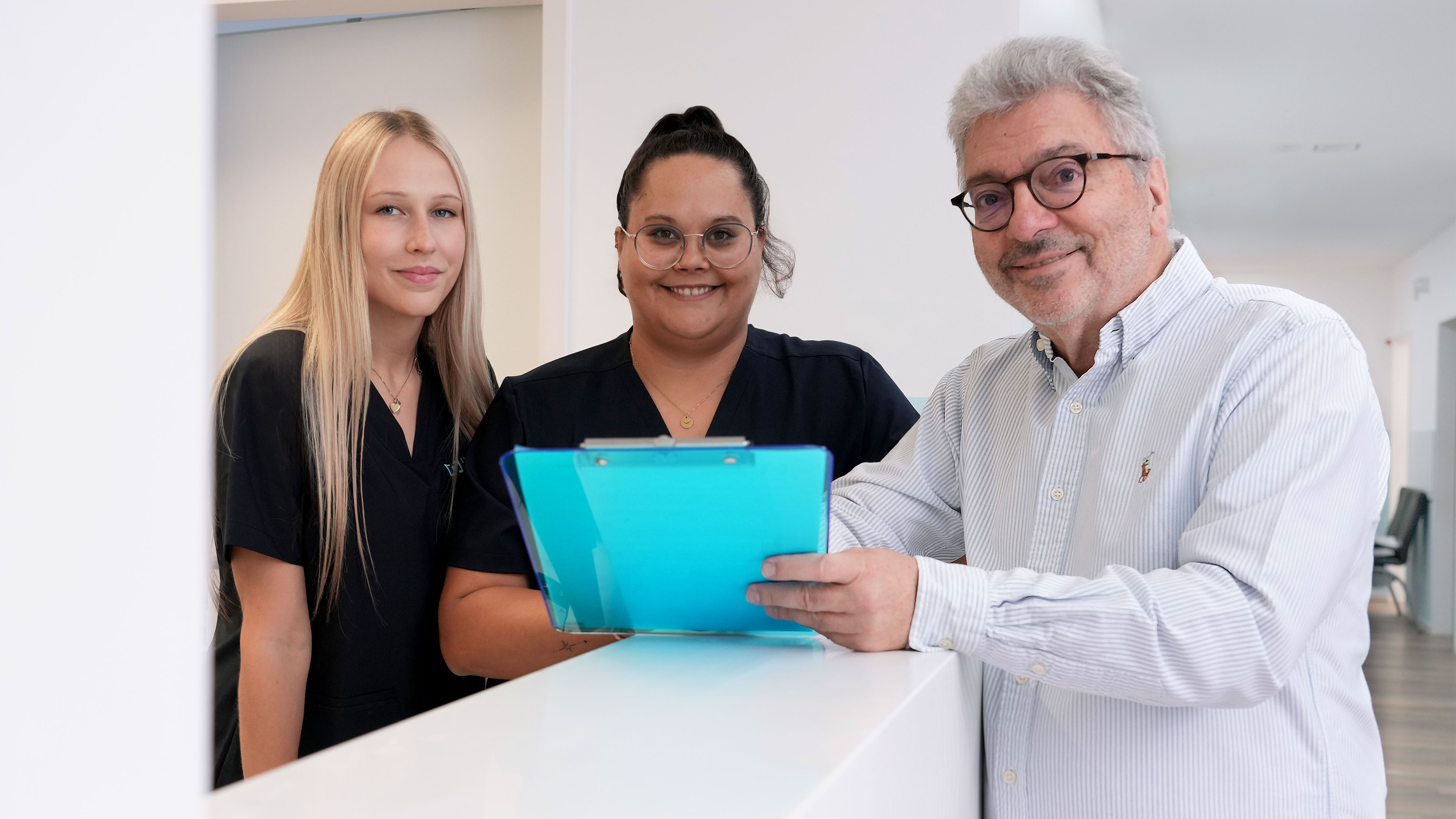 Dr. med. Andreas Forster freundlich lächelnd mit Patientenakte neben zwei Mitarbeiterinnen am Empfangstresen im Lungenzentrum Darmstadt, Standort Fachärztehaus am Klinikum Darmstadt